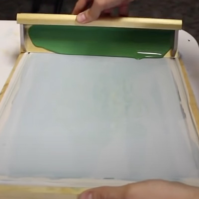 Applying photosensitive emulsion to a silk screen with a scoop coater.